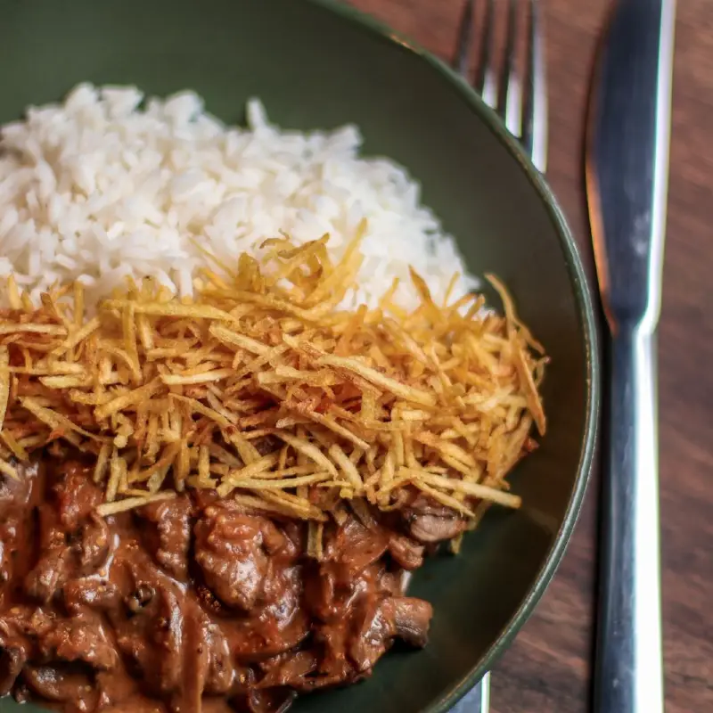 Strogonoff de filé com arroz e batata palha em bowl escuro